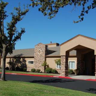 A single-story suburban building with a prominent entrance and surrounding trees under a clear blue sky.