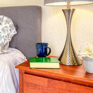 A cozy bedroom scene with a nightstand featuring a book, mug, and elegant lamp.