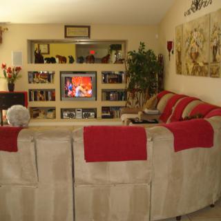 A cozy living room with a large sofa facing a television, surrounded by shelves and decor.