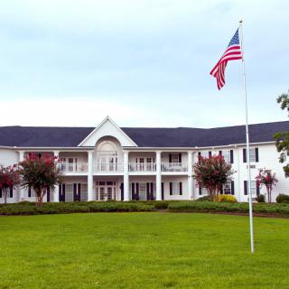 A large mansion with colonial architecture, featuring a prominent American flag on the lawn.