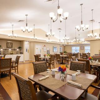 A well-lit dining room with neatly arranged tables and chairs, adorned with elegant chandeliers and a wooden floor.