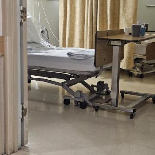 A view of a patient room in a hospital, featuring an unoccupied hospital bed and medical equipment.