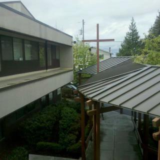 A view of a modern building with a cross, surrounded by trees under an overcast sky.