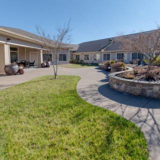 A sunny courtyard surrounded by buildings with a paved walkway and green lawn.