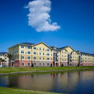 A modern apartment building by a lake with a clear blue sky and clouds.