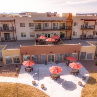 A modern apartment complex with outdoor seating areas and red umbrellas, showcasing its spacious balconies and patio.