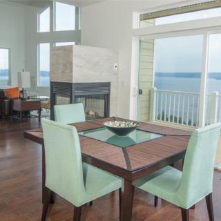 A modern dining room with a table and chairs, featuring large windows offering an ocean view.