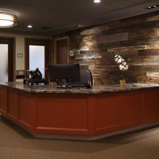 A modern office reception area with a wooden desk and wall paneling.