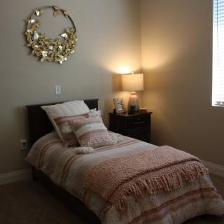 A cozy bedroom with a single bed, decorative pillows, a lit lamp on the nightstand, and wall decor above the bed.
