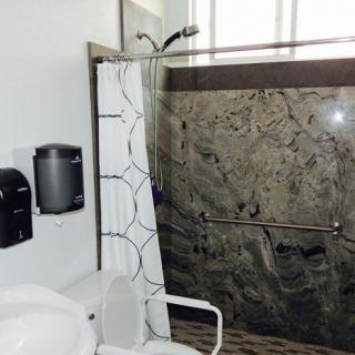 An accessible bathroom featuring a shower with a grab bar, toilet, and curtain.
