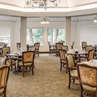 An elegant dining room with neatly arranged tables and chairs, featuring large windows and a chandelier.