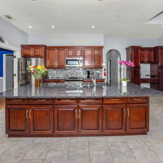 A spacious kitchen featuring wood cabinets, a large central island with a granite countertop, stainless steel appliances, and decorative flowers.