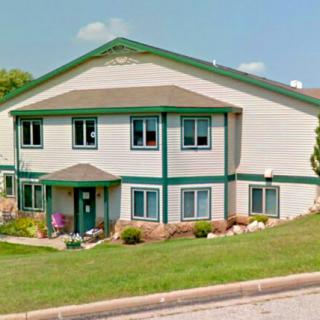 A two-story residential building with green trim and a well-maintained lawn.