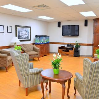 A cozy waiting room with comfortable seating, a television, and an aquarium, decorated with indoor plants and wooden flooring.