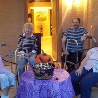 A group of seniors celebrating Halloween, gathered around a table with candy and festive decorations.