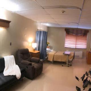 A spacious and well-lit hospital patient room featuring a bed, comfortable seating area, and curtains for privacy.