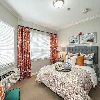 A cozy bedroom with a neatly made bed, vibrant curtains, and decorative pillows.