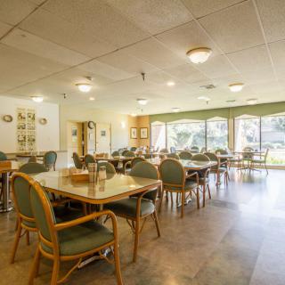 An empty dining area with neatly arranged tables and chairs, featuring large windows for natural light.
