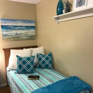 A cozy bedroom corner featuring a beach-themed painting, matching pillows, and a decorative shelf.