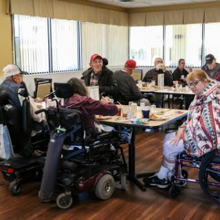 A group of individuals in wheelchairs enjoying a meal together in a dining area.