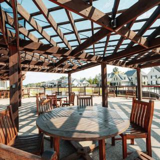 A sunny patio with wooden tables and chairs under a pergola, casting intricate shadows.