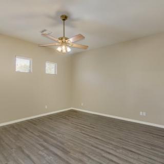 An empty room with a ceiling fan, laminate flooring, and two small windows.