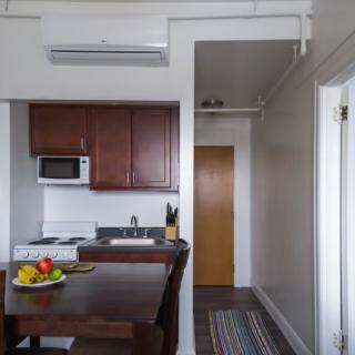 A modern apartment kitchen with a small dining area, featuring a microwave, fruit bowl, and air conditioning.