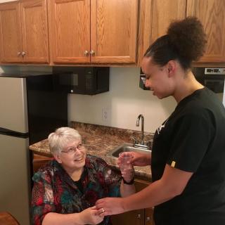 A caretaker assists an elderly woman in the kitchen, sharing a moment of connection.