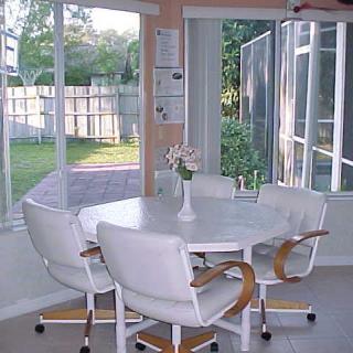 A bright dining area with large windows letting in natural light, featuring a round table and white chairs.