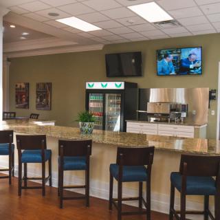A cozy cafe interior with a bar counter and chairs, featuring a refrigerator and television.