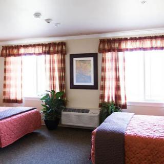 A hotel room featuring two beds, large windows with curtains, and tasteful decoration.
