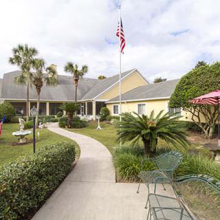 A picturesque garden pathway leads to a building, adorned with palm trees and outdoor seating, under an American flag.