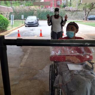 A person in a wheelchair is being assisted outside, while another individual stands behind them with their hands raised.
