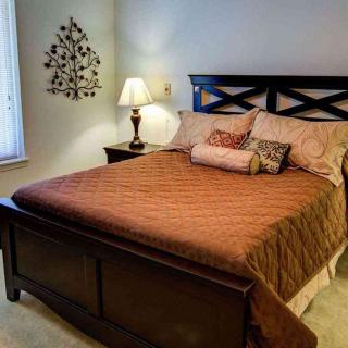 A cozy bedroom with a neatly made bed, accented by decorative pillows and a side lamp.
