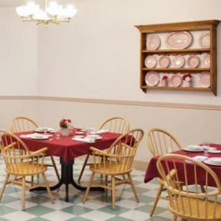A cozy dining area with tables set for a meal, featuring red tablecloths and wooden chairs.