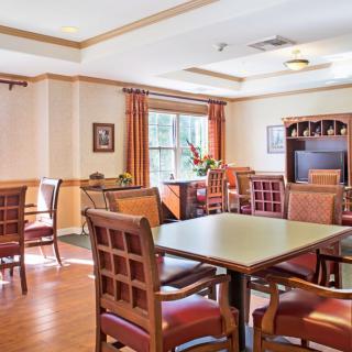 A well-lit dining room with wooden tables and chairs, featuring a large window with curtains.