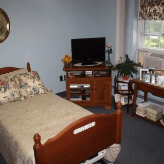 A cozy bedroom with a bed, television stand, potted plant, and window.