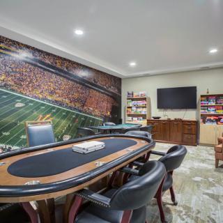 A sports-themed game room featuring a poker table and chairs, with a large mural on the wall and a television.