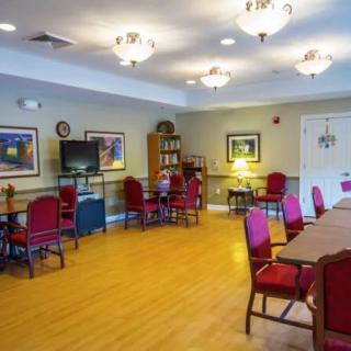 A spacious community room with red chairs, tables, a television, and a bookshelf.