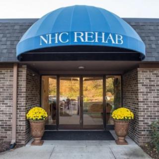 Entrance of a rehabilitation center with a blue awning labeled 'NHC Rehab'.
