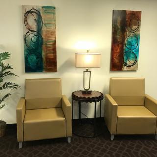 A cozy waiting area with two beige chairs, abstract art on the walls, and a lamp on a small round table.