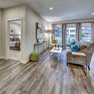 A modern living room with hardwood floors and stylish furniture, featuring a cozy seating area and large windows letting in natural light.