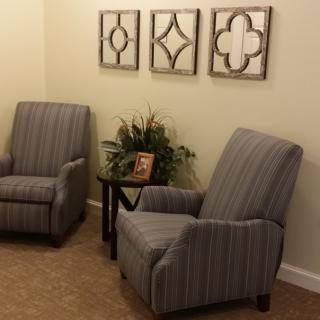 A cozy living room corner with two striped chairs, decorative wall art, and a small side table with a plant.