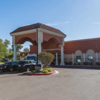 A large building with an arched entrance and parking lot in front, captured on a sunny day.