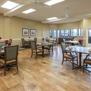 A spacious dining room with neatly arranged tables and chairs, featuring a warm wooden floor and large windows.
