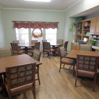 A cozy dining area with wooden tables and chairs, decorated with curtains and plants.