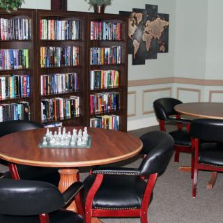 A cozy library corner with bookshelves and a chess board on a round table.