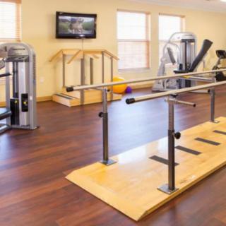 A rehabilitation gym featuring fitness equipment including parallel bars and a treadmill.