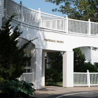 A white architectural structure with a curved entrance and railing, surrounded by trees.