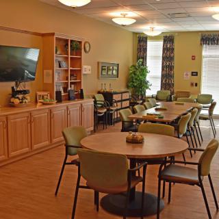 A comfortable dining area with tables and chairs, featuring a television and shelving for decor.